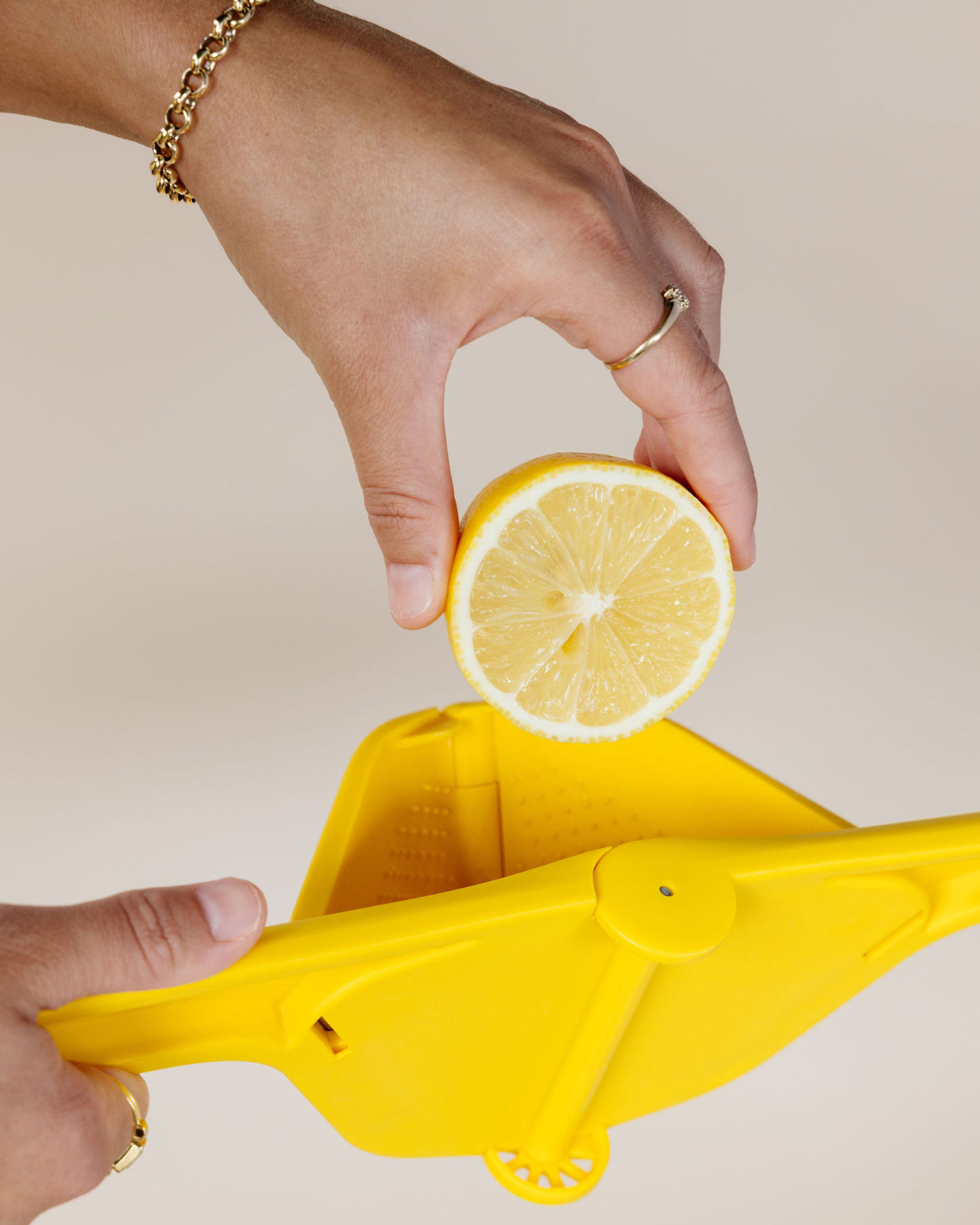 A person's hands using a yellow Byroncello lemon squeezer with a lemon slice placed on it.